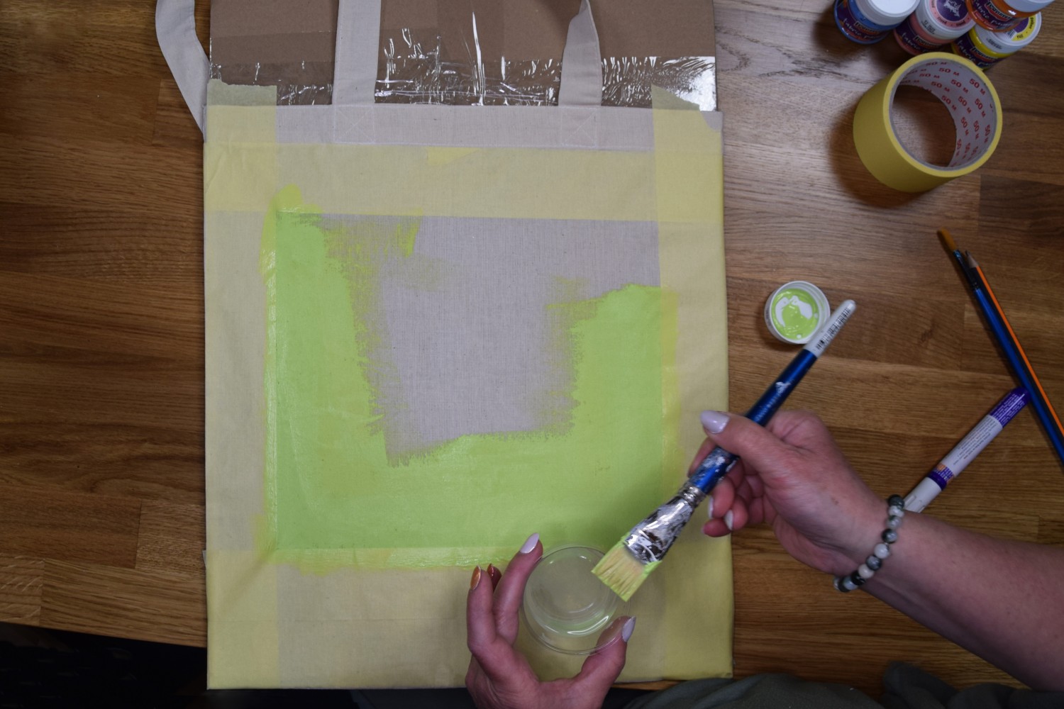 Žena nanáša na prázdne miesto vytvorené lepiacou páskou zelenú farbu na textil.